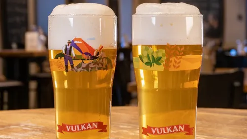 Two beer glasses with foam on wooden table.