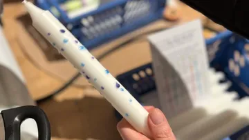 Hand hält weiße Kerze mit blauen Punkten.