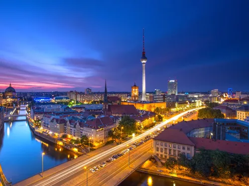 Stadtansicht Berlins bei Dämmerung, beleuchtete Gebäude und Fluss.