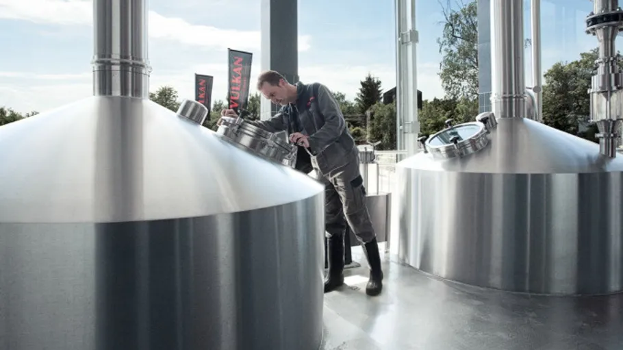 Person inspecting large brewing vats indoors.