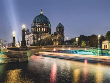 Berlin Cathedral reflects in water as boats pass by.