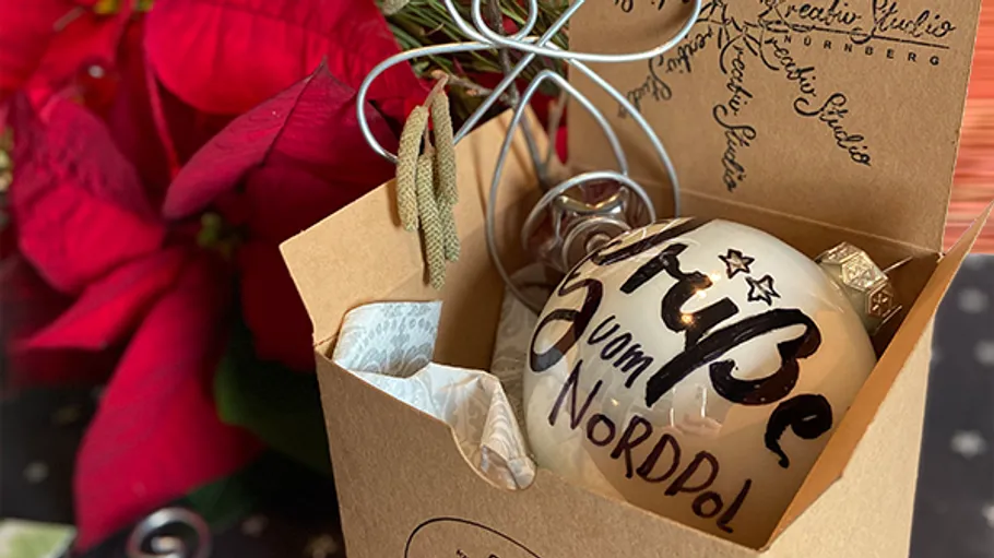 Glass ornament in box beside poinsettias.