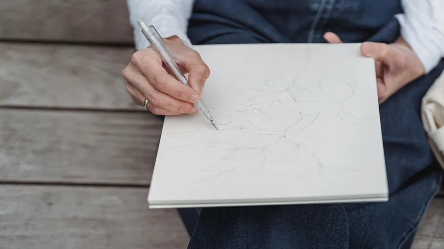 Person sketching on a notebook outdoors.
