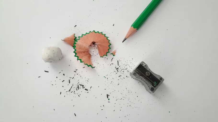 Pencil, sharpener, shavings on white surface.