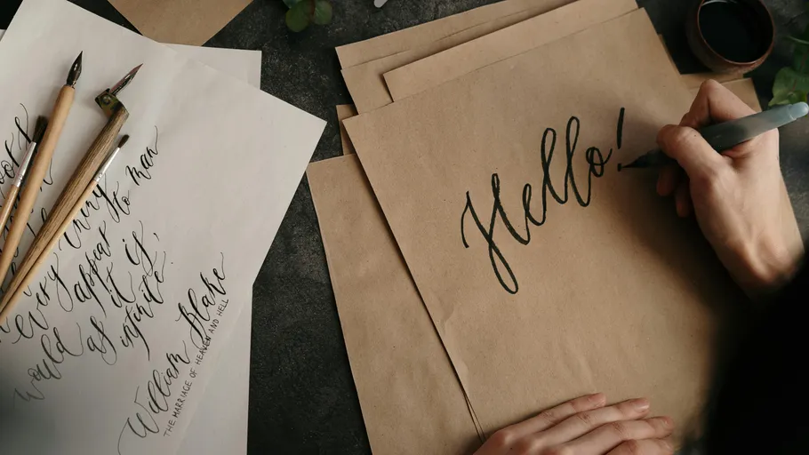 Hand writing 'Hello' on brown paper sheets.