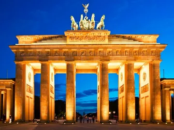 Brandenburg Gate glows at night, surrounded by a blue sky.