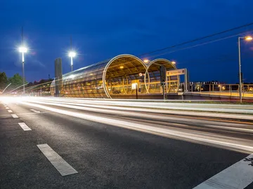 Modern bus stop lights up at night as cars pass by.