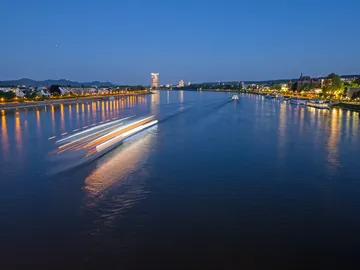 Boat sails on a quiet river with an illuminated waterfront.