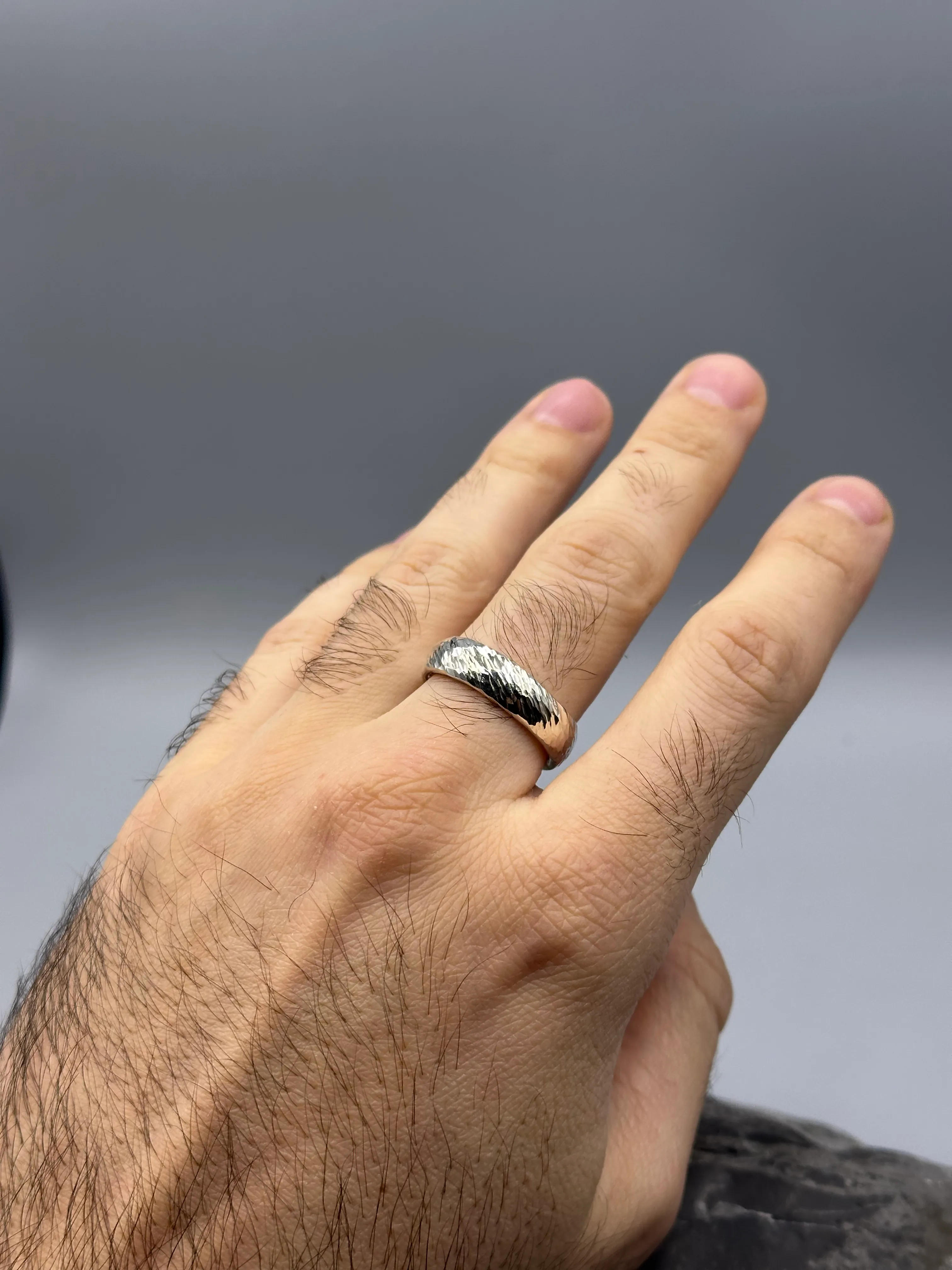 Hand trägt Silberring, grauer Hintergrund.