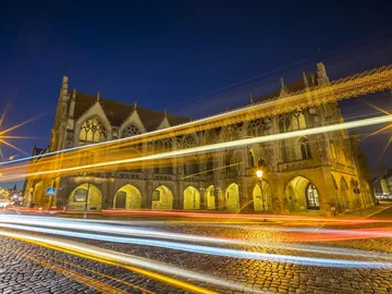 Historic building glows at night as cars pass by.