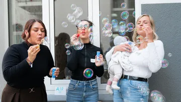 Drei Frauen blasen Seifenblasen vor Gebäude.