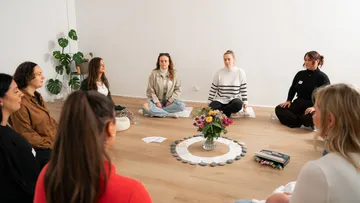 Menschen sitzen im Kreis und meditieren drinnen.