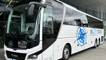 Weißer Reisebus vor modernem Gebäude geparkt.