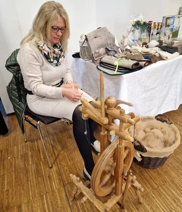 Frau spinnt Wolle an einem Spinnrad.