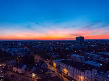 Stadtansicht bei Sonnenuntergang, Gebäude und Straßen beleuchtet.