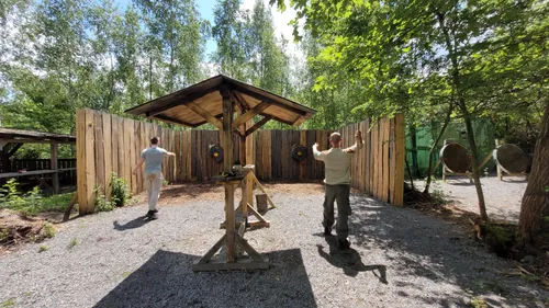 Two men axe throwing in wooded area.