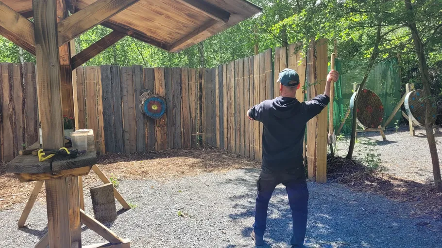 Man aiming bow at wooden target outdoors.