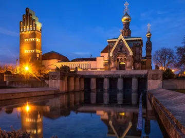 Zwei Gebäude reflektieren im Wasser bei Nachtbeleuchtung.