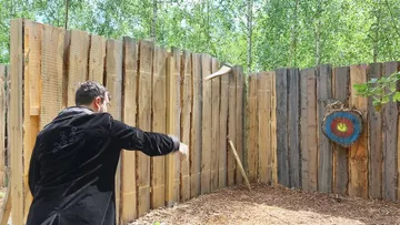 Person wirft Axt auf Holzscheibe im Freien.