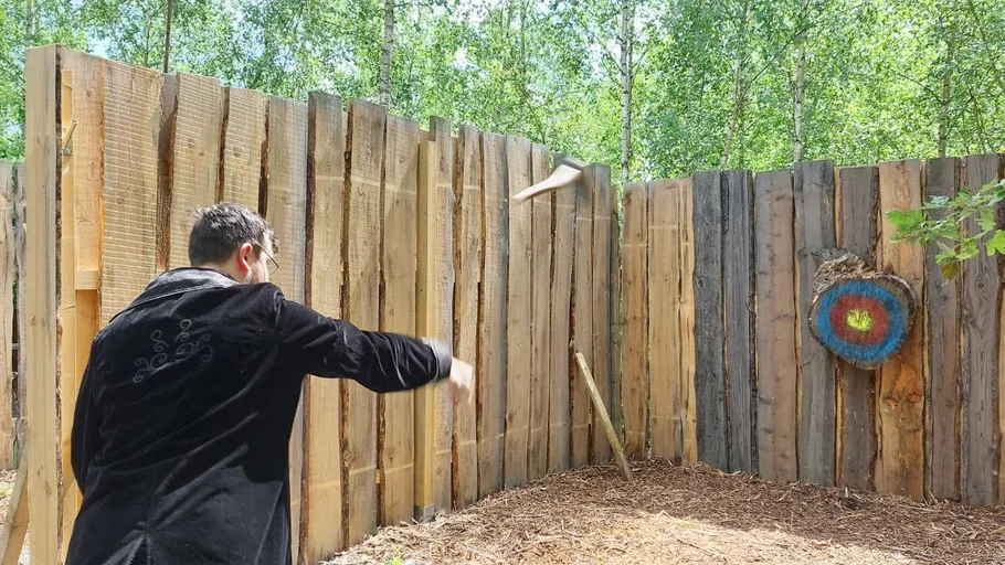 Person throwing axe at wooden target outdoors.