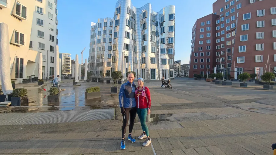 Two people posing in front of modern buildings.