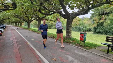 Zwei Personen joggen in einem baumbestandenen Park.