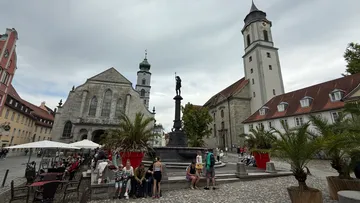 Menschen sitzen am Brunnen, historische Gebäude rundherum.