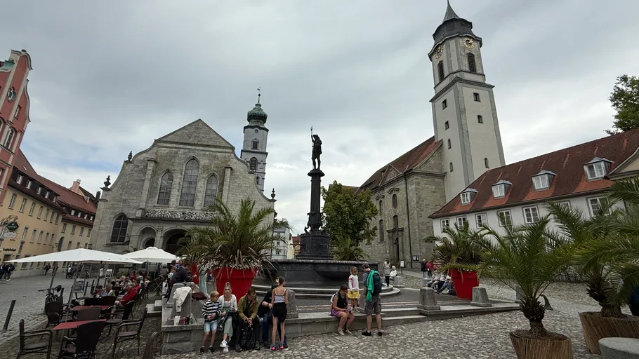People sitting near fountain, historic buildings around.