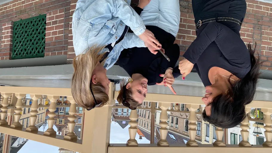 Drei Frauen reden auf einem Balkon mit Stadtblick.