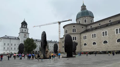 Tourists with umbrellas near large sculptures and buildings.