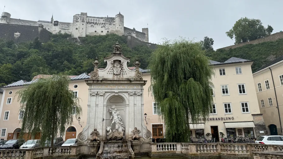 Brunnen mit Festung auf Hügel im Hintergrund.