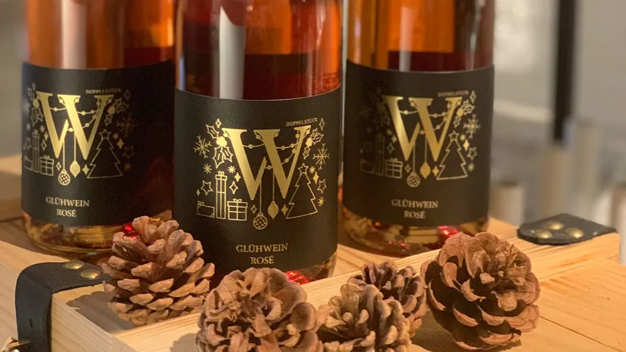 Three bottles of Glühwein with pinecones on wooden surface.
