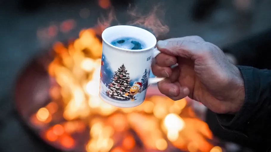 Hand holding mug near outdoor fire.
