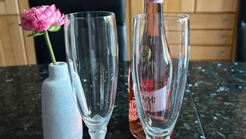 Two glasses with rose and bottle on table.