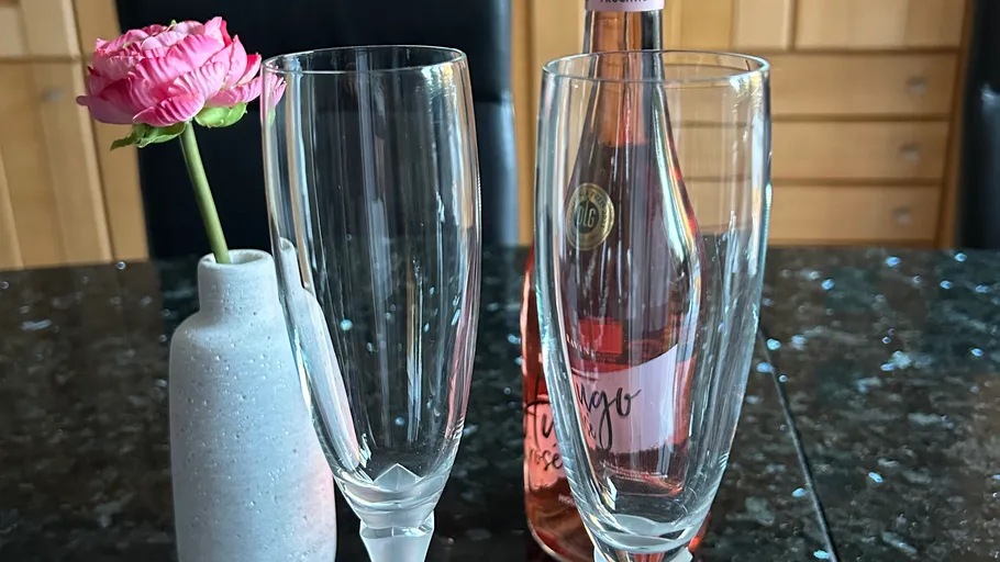 Zwei Gläser mit Rose und Flasche auf Tisch.