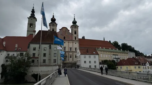 People walking on bridge towards historic buildings.