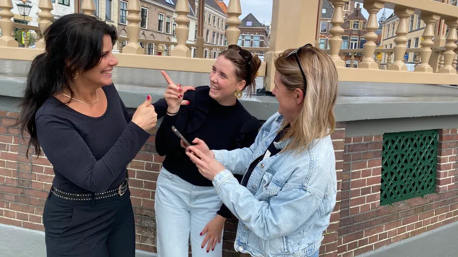Three women talking, wooden railing, urban background.