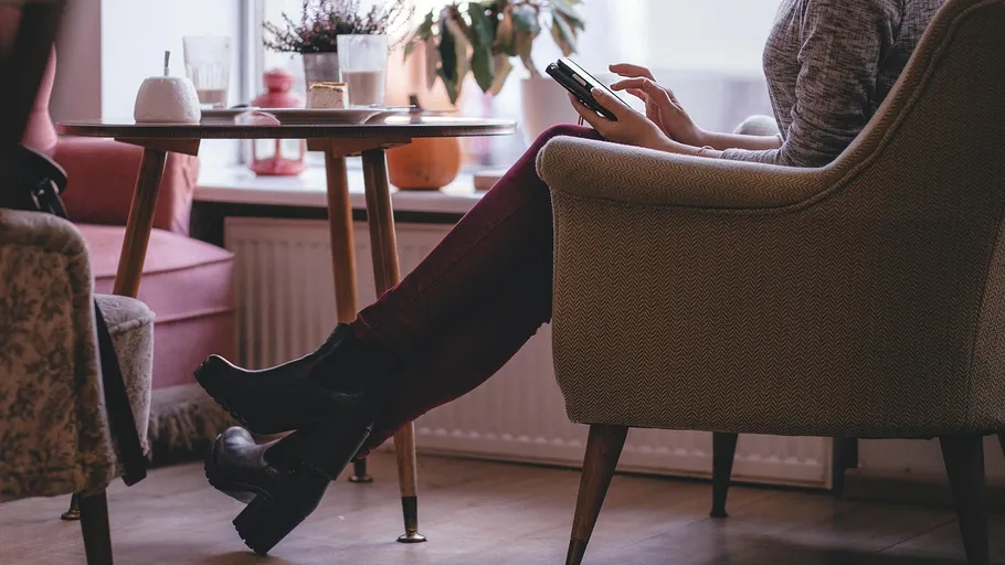 Person sitzt auf Stuhl und nutzt Smartphone drinnen.