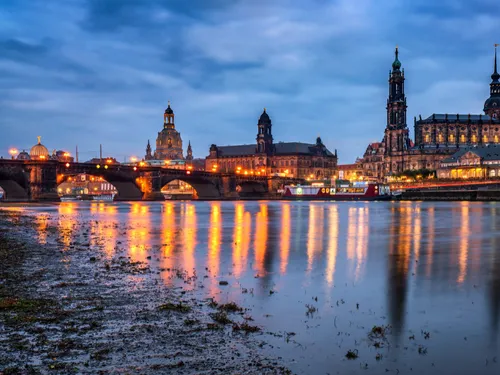 Brücke reflektiert Lichter in ruhigem Fluss bei Dämmerung.