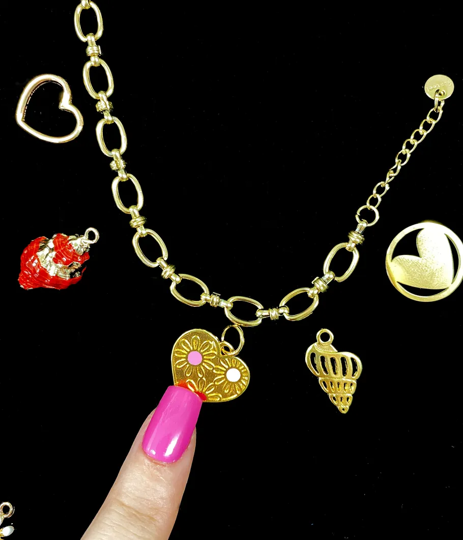 Gold heart charms on a chain with finger.