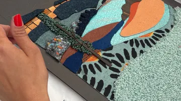 Hand arranging colorful textile collage art.