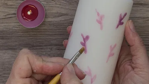 Person painting floral designs on a white candle.