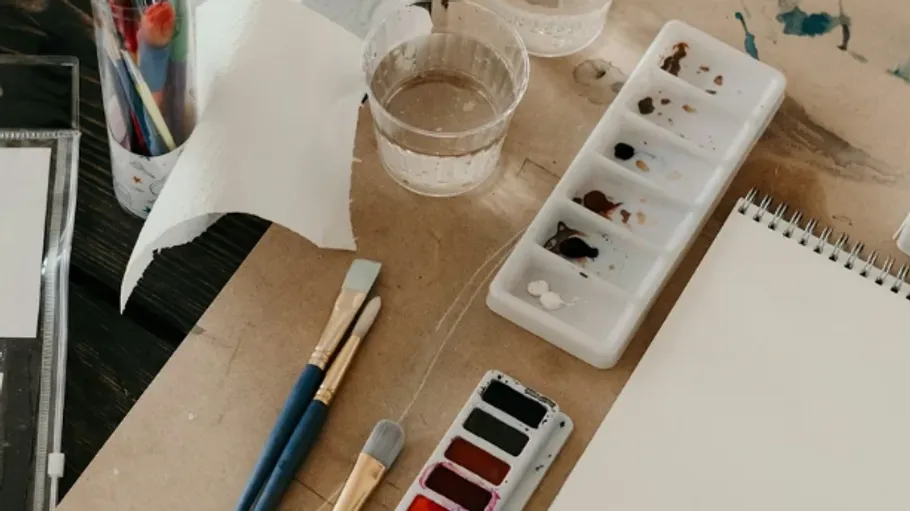 Kunstmaterialien auf Tisch, einschließlich Pinsel und Farben.
