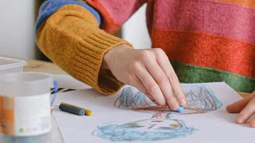Person zeichnet buntes Portrait mit Pastellkreiden.