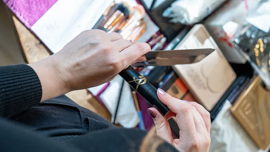 Person holding makeup brush and knife, cluttered table.