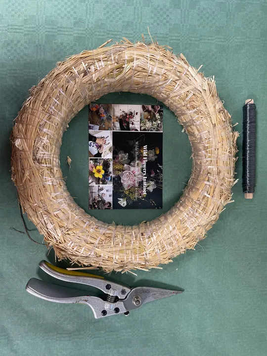 Straw wreath, wire coil, and pruners on table.
