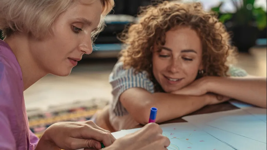 Two women drawing together on paper.