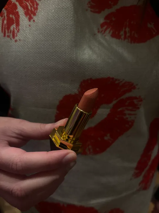 Hand hält Lippenstift, rote Lippen im Hintergrund.