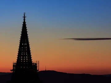 Spitzdach erhebt sich vor einem bunten Sonnenuntergangshimmel.