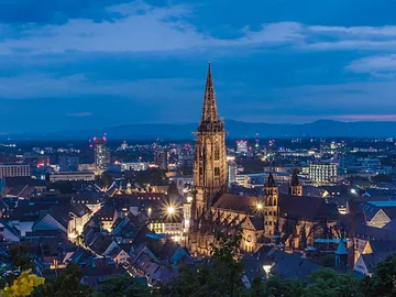 Gothic church glows over illuminated cityscape at night.